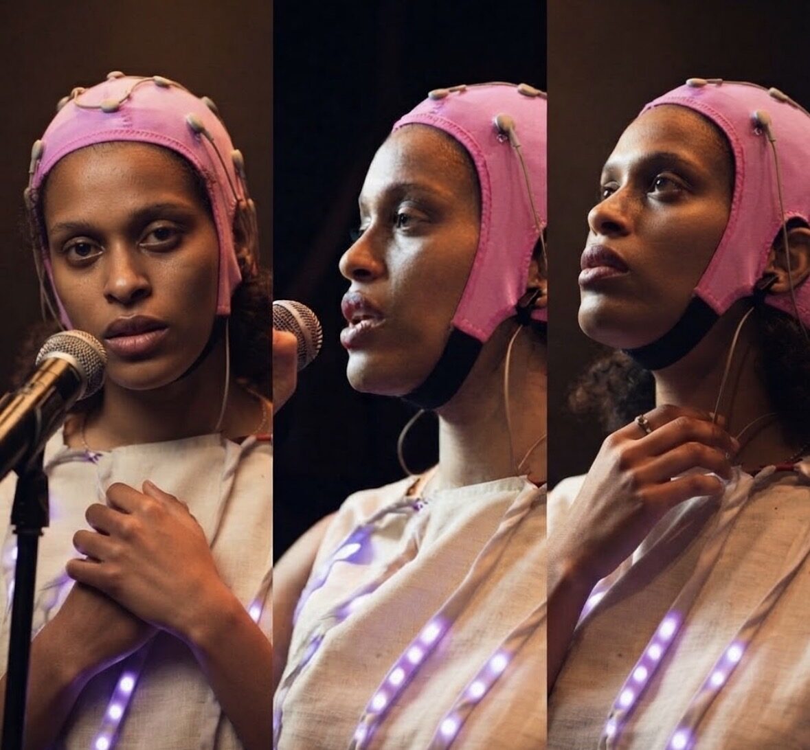 Three frames of a performer in a pink EEG cap and a light-studded costume singing into a microphone on stage.