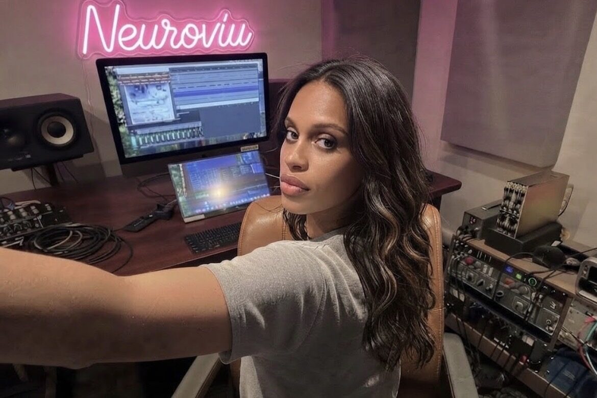 Ashlei Lewis in a music studio beneath a pink neon NeuroViu sign, monitors and synthesizers around her.
